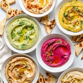 five bowls of homemade hummus on a board